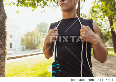One young handsome caucasian man in sportswear posing with rope at crossfit ground on bright summer day. 81106701