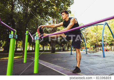 One young handsome caucasian man in sportswear training, exercising on crossfit ground outdoors on bright summer day. One young handsome caucasian man in sportswear training, exercising on crossfit ground outdoors on bright summer day. 81106803