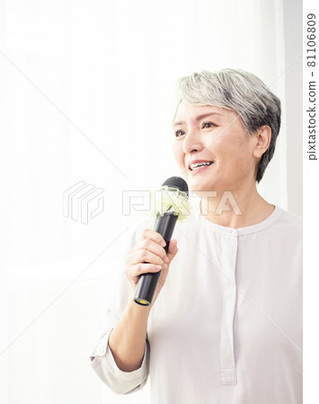 快樂的亞洲成熟女人用麥克風唱歌. 81106809