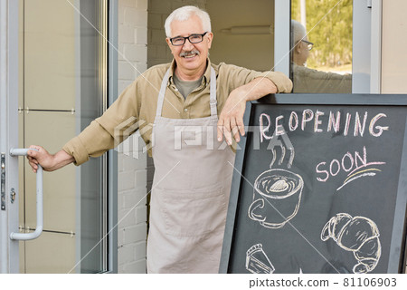 Happy mature owner of bakery standing by entrance and opening door 81106903
