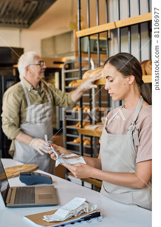 Busy female worker of bakery looking through receits 81106977