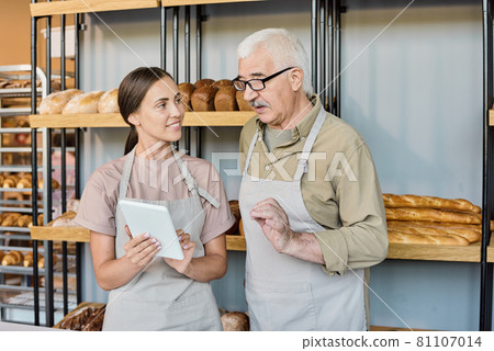 Young and senior bakers discussing new online assortment 81107014