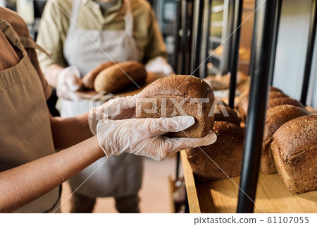 Gloved hands of young woman holding fresh loaf of bread Gloved hands of young woman holding fresh loaf of bread 81107055