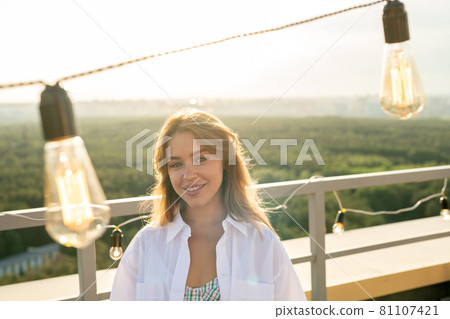 Young attractive woman standing on rooftop patio decorated with illumination Young attractive woman standing on rooftop patio decorated with illumination 81107421
