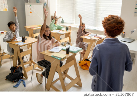 Young teacher standing in front of kids raising hands Young teacher standing in front of kids raising hands 81107807
