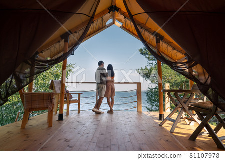 Rear view of amorous couple standing close to each other and looking at ocean Rear view of amorous couple standing close to each other and looking at ocean 81107978