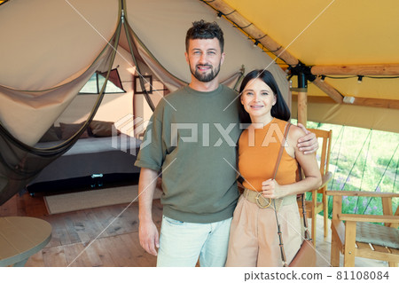 Happy young man and woman standing against interior of their glamping house Happy young man and woman standing against interior of their glamping house 81108084