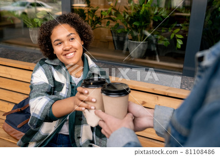 Happy teenage girl taking glass of coffee offered by her boyfriend Happy teenage girl taking glass of coffee offered by her boyfriend 81108486