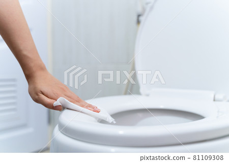 close up hand cleaning Toilet seat by a wet wipe with alcohol spray in public restroom for coronavirus prevention and hygiene before using 81109308