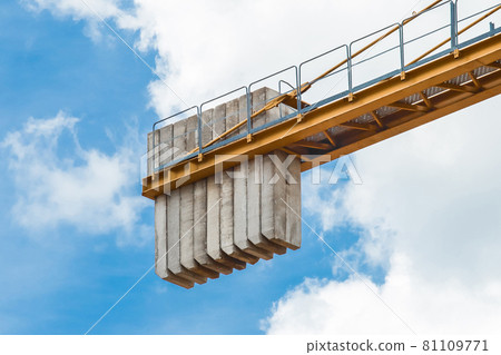 A counterweight of concrete blocks on the tail of a tower crane industrial equipment against a blue sky. Close-up A counterweight of concrete blocks on the tail of a tower crane industrial equipment against a blue sky. Close-up 81109771