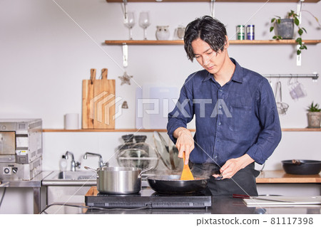 Image of a young man cooking in an apron cooking in the kitchen 81117398