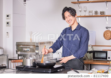 Image of a young man cooking in an apron cooking in the kitchen 81117400