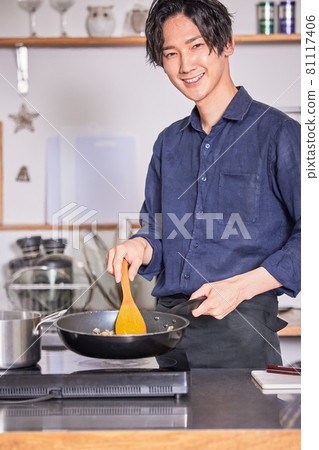 Image of a young man cooking in an apron cooking in the kitchen Image of a young man cooking in an apron cooking in the kitchen 81117406
