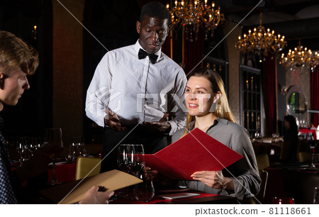 Couple with menu is giving order to african-american waiter in fashionable restaurant Couple with menu is giving order to african-american waiter in fashionable restaurant 81118661