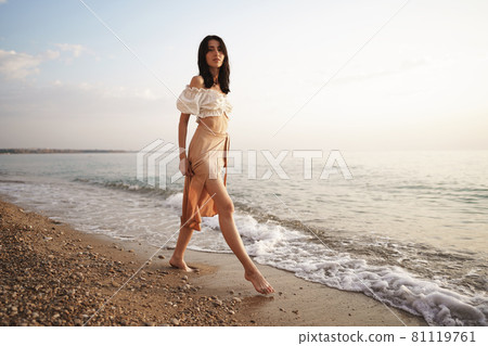 Lonely young woman walks on the seashore at sunset 81119761