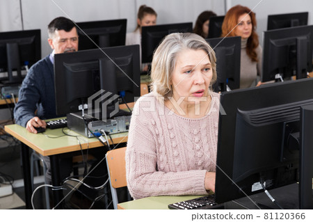 Young and older businesswomen and businessmen in open plan office 81120366