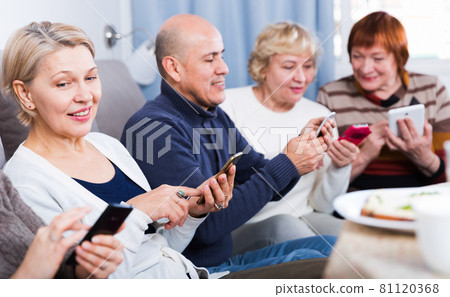 Mature friends are sitting on sofa and chatting on phone 81120368