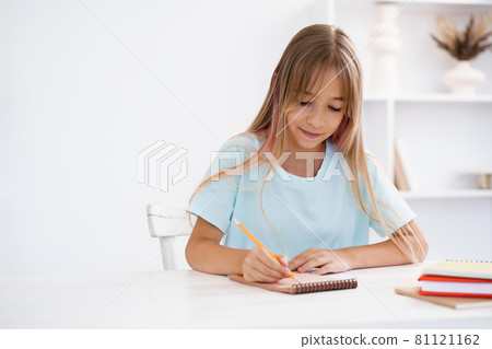 Teenage girl making notes in notepad, doing homework at table at home 81121162