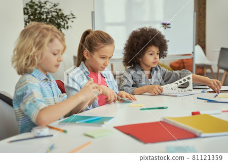 Cute diverse kids sitting together at the table while studying in elementary school classroom 81121359