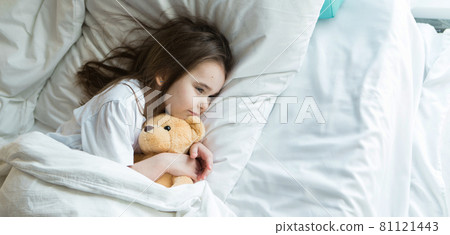 baby lying in bed with Taddy Bear. Little girl sleeps with knitted toy 81121443