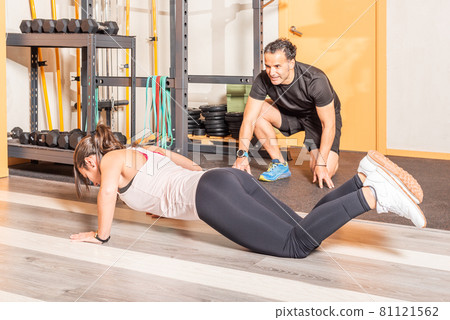 Woman doing push ups with trainer in the gym Woman doing push ups with trainer in the gym 81121562