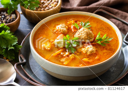 Soup close-up. Tomato-lentil soup with meatballs and vegetables on a dark slate table top. 81124617