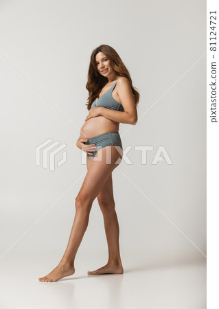Portrait of beautiful pregnant woman in lingerie isolated over grey studio background. Natural beauty, happy motherhood, femininity concept. 81124721