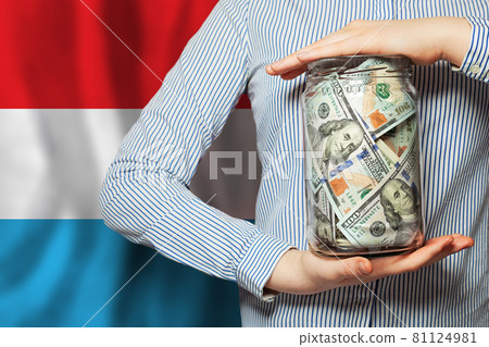 Hands holds US dollars banknotes against flag of Luxembourg Hands holds US dollars banknotes against flag of Luxembourg 81124981