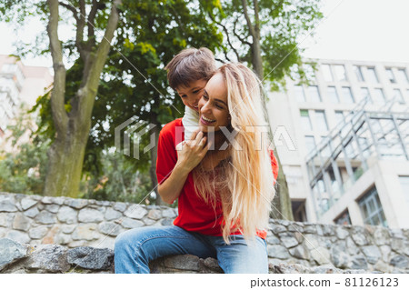 Happy mother and little cute son strolling at street, public park in summer time, outdoors. Family time, togehterness, parenting and happy childhood concept. 81126123