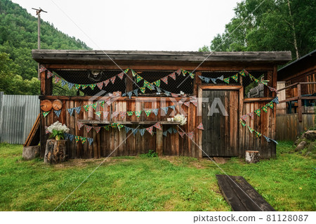 Wooden shed or hut is decorated with colorful triangle flags and bouquet of white gypsophila flowers. Preparing for the celebration of the holiday outdoors in the hot summer Wooden shed or hut is decorated with colorful triangle flags and bouquet of white gypsophila flowers. Preparing for the celebration of the holiday outdoors in the hot summer 81128087
