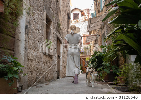Rear view of beautiful blonde young female traveler wearing straw sun hat sightseeing and enjoying summer vacation in an old traditional costal town at Adriatic cost, Croatia 81128546