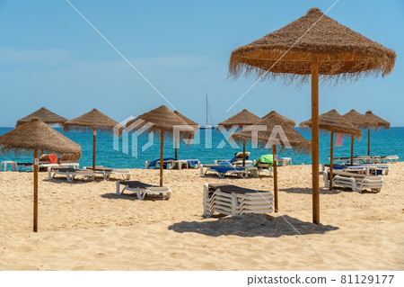 View of the luxury beach on the sea with sun loungers and umbrellas, in the tourist zone of the tropics. In the background is a yacht sailing ship. View of the luxury beach on the sea with sun loungers and umbrellas, in the tourist zone of the tropics. In the background is a yacht sailing ship. 81129177