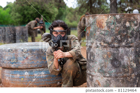Female paintball player aiming and shooting with gun at opposing team Female paintball player aiming and shooting with gun at opposing team 81129464