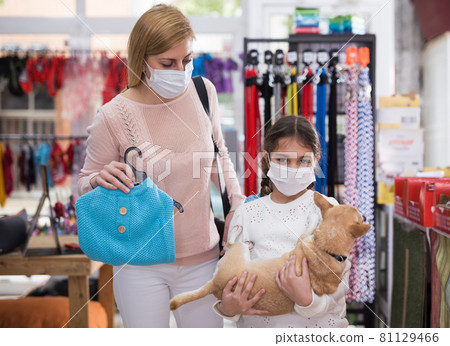Woman in mask in pet store during shopping with her daughter with dog Woman in mask in pet store during shopping with her daughter with dog 81129466