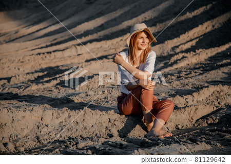 Young beautiful lonely woman with long hair with straw hat. A lonely girl goes down the sand dunes. Summer fashion poartrait outdoor. 81129642