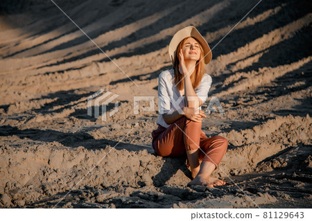 Young beautiful lonely woman with long hair with straw hat. A lonely girl goes down the sand dunes. Summer fashion poartrait outdoor. 81129643