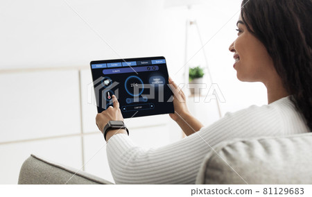 Happy african american woman regulating room temperature via smart home 81129683