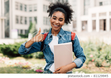 African American Female Student Gesturing Thumbs-Up Posing Near University Building 81129945