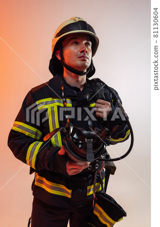 Close-up. One male firefighter dressed in uniform posing over orange background in neon lights. 81130604