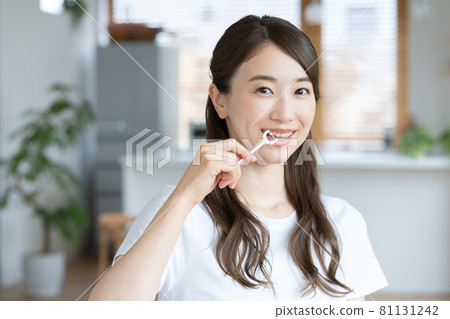 A young woman cleaning her teeth with a toothpick in her living room A young woman cleaning her teeth with a toothpick in her living room 81131242