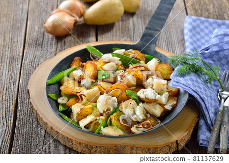 Fried potatoes with pieces of halibut fillet, sugar peas and onion rings, served in a frying pan 81137629