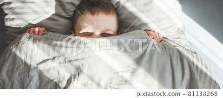 boy sleep in the bed. child lies on pillow and covers his face with a blanket. banner 81138268