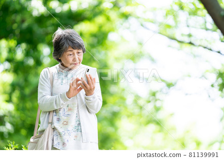 A senior woman who operates a smartphone, an old woman who touches a smartphone outdoors 81139991