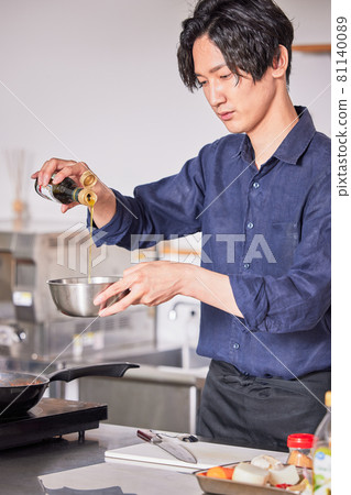 A young man in an apron who puts olive oil in a bowl. 81140089