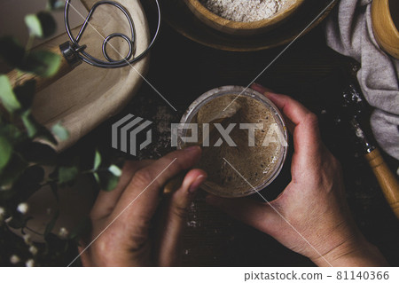 Starter sourdough. Female hands holding a jar with sourdough over wooden background. Starter sourdough. Female hands holding a jar with sourdough over wooden background. 81140366