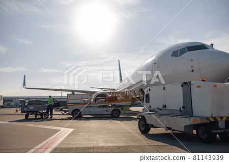 Worker loading baggage on conveyor belt to an airplane outdoors on a daytime Worker loading baggage on conveyor belt to an airplane outdoors on a daytime 81143939