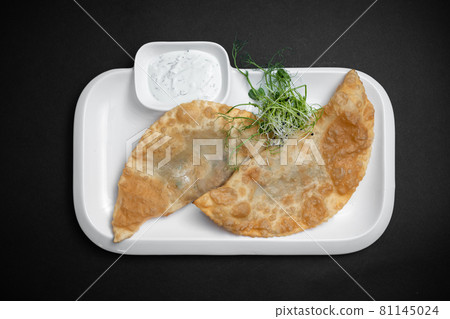 cheburek or fried dough pie with meat feeling and sauce on black background cheburek or fried dough pie with meat feeling and sauce on black background 81145024