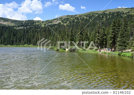 Distant hikers on shore of Hassell Lake in Arapaho National Forest, Colorado. 81146102