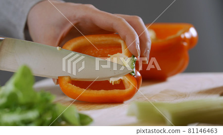 Woman's hands slicing sweet Red Bell Pepper on a wooden cutting board (UHD, 4K) beautiful shot with soft focus. Healthy food concept. 81146463