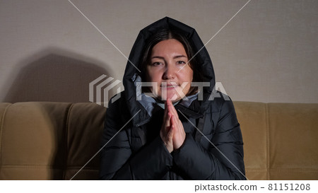 Lady in warm jacket with hood tries to heat hands on sofa Lady in warm jacket with hood tries to heat hands on sofa 81151208